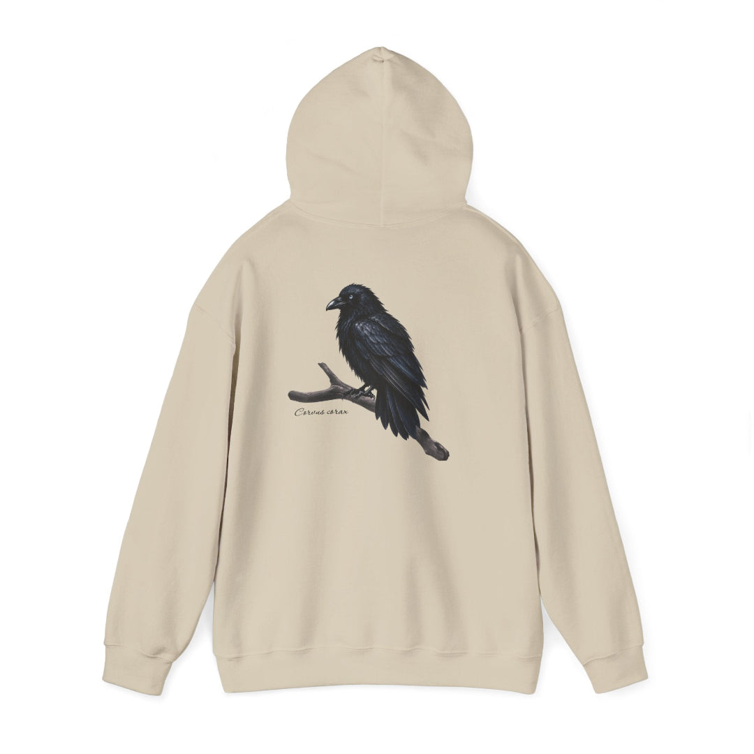 Hippuli brändin beige huppari, jossa on maalattu kuva puun oksalla istuvasta Corvus corax -korpista. Kuvassa huppu ylhäällä.
