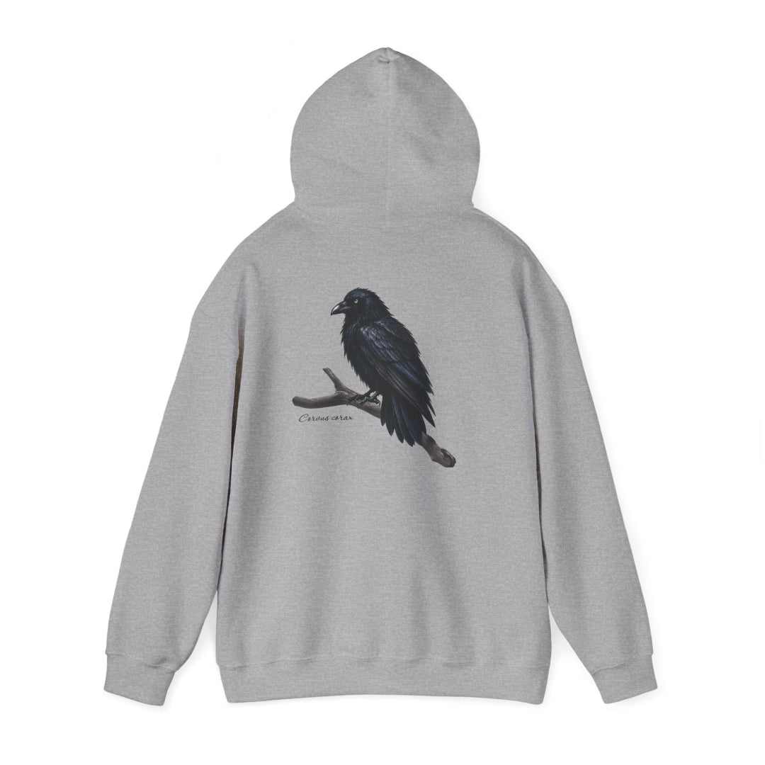 Hippuli brändin harmaa huppari, jossa on maalattu kuva puun oksalla istuvasta Corvus corax -korpista. Kuvassa huppu ylhäällä.